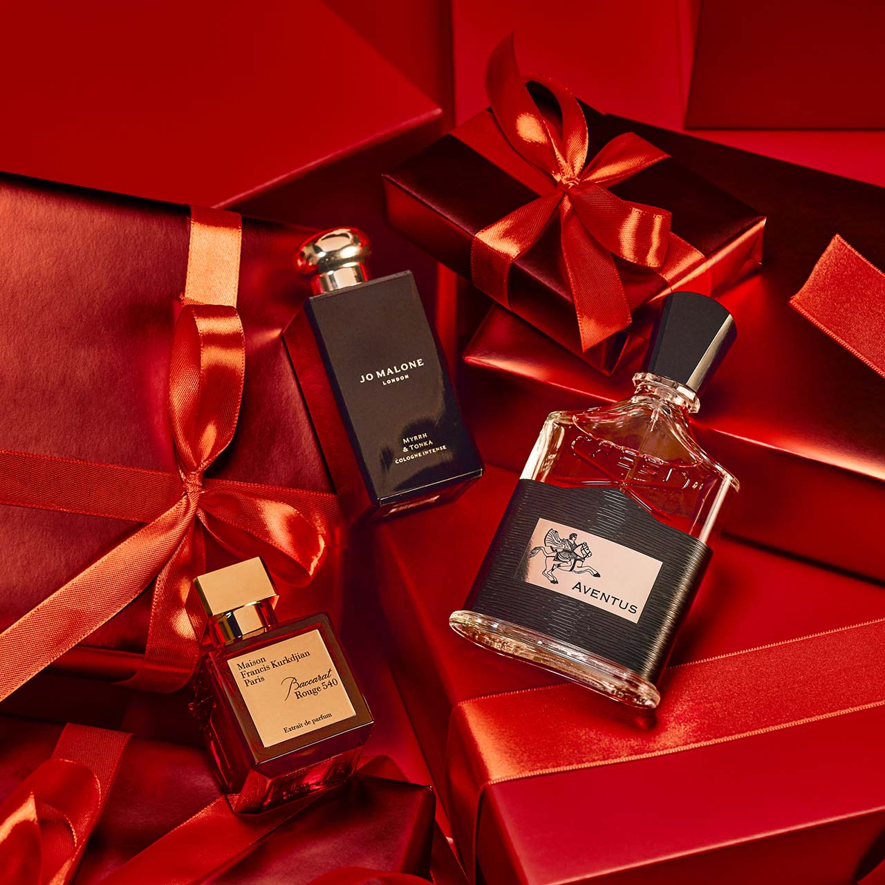 Bottles of perfume are surrounded by red gift boxes with matching ribbons.