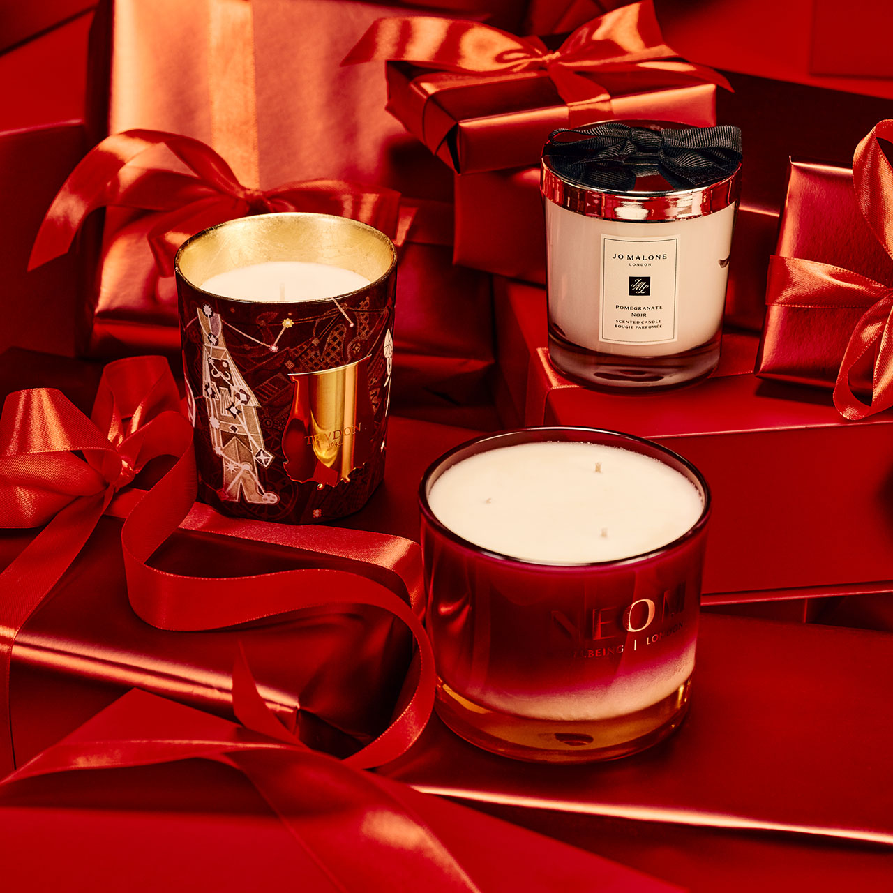 Three decorative candles placed among wrapped red gifts with ribbon.