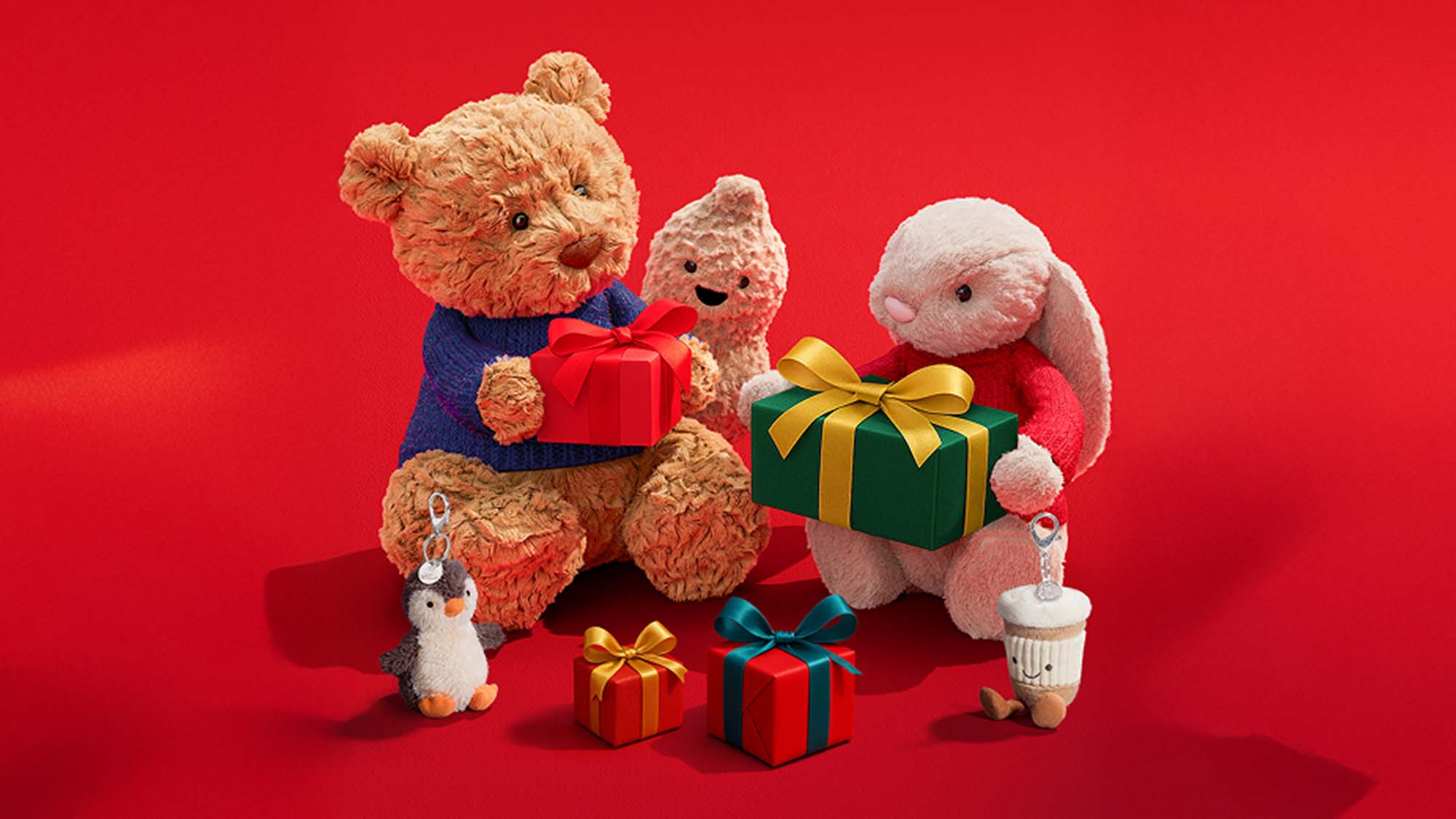 Plush toys, including a bear and rabbit, sit on a red background holding wrapped gifts.