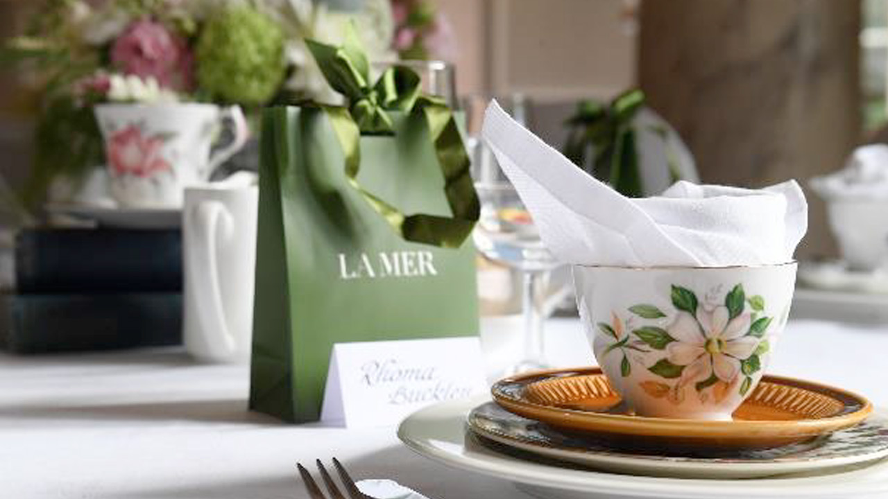 Elegant table setting with a floral teacup, napkin, and a green gift bag.