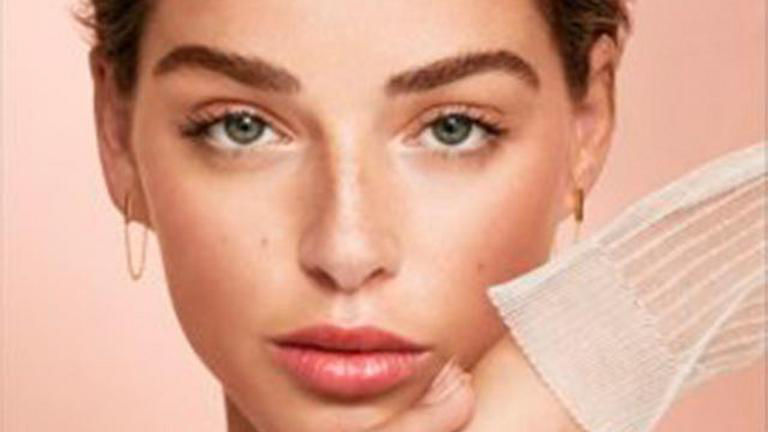 Close-up of a woman with hoop earrings and neutral makeup against a soft pink background.