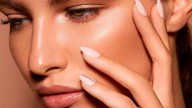 Close-up of a person with smooth skin, minimal makeup, and manicured nails touching their face.
