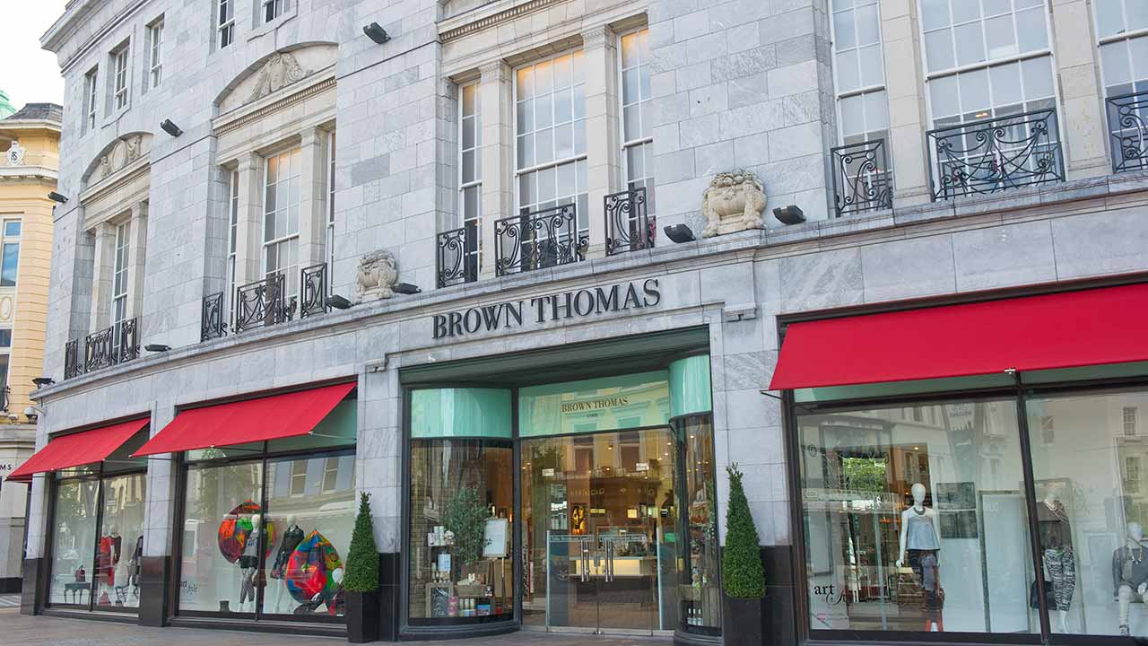 A stone building with large windows, red awnings, and a sign reading 'Brown Thomas' above the entrance.