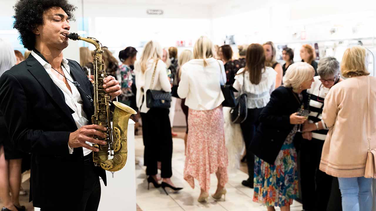 
A saxophonist plays in a busy indoor event with people socializing in the background.
